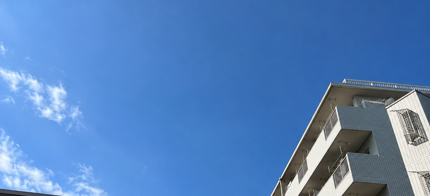 青空を背景にアパートを見上げる