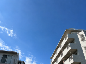 青空を背景にアパートを見上げる